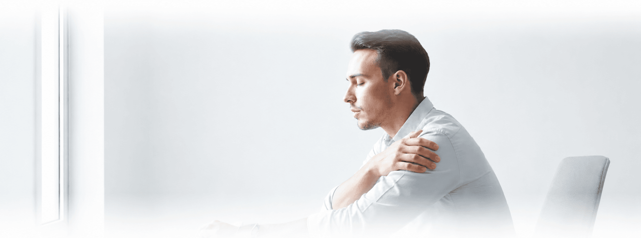 A man pauses at his desk, hand on his shoulder, smartwatch on his wrist